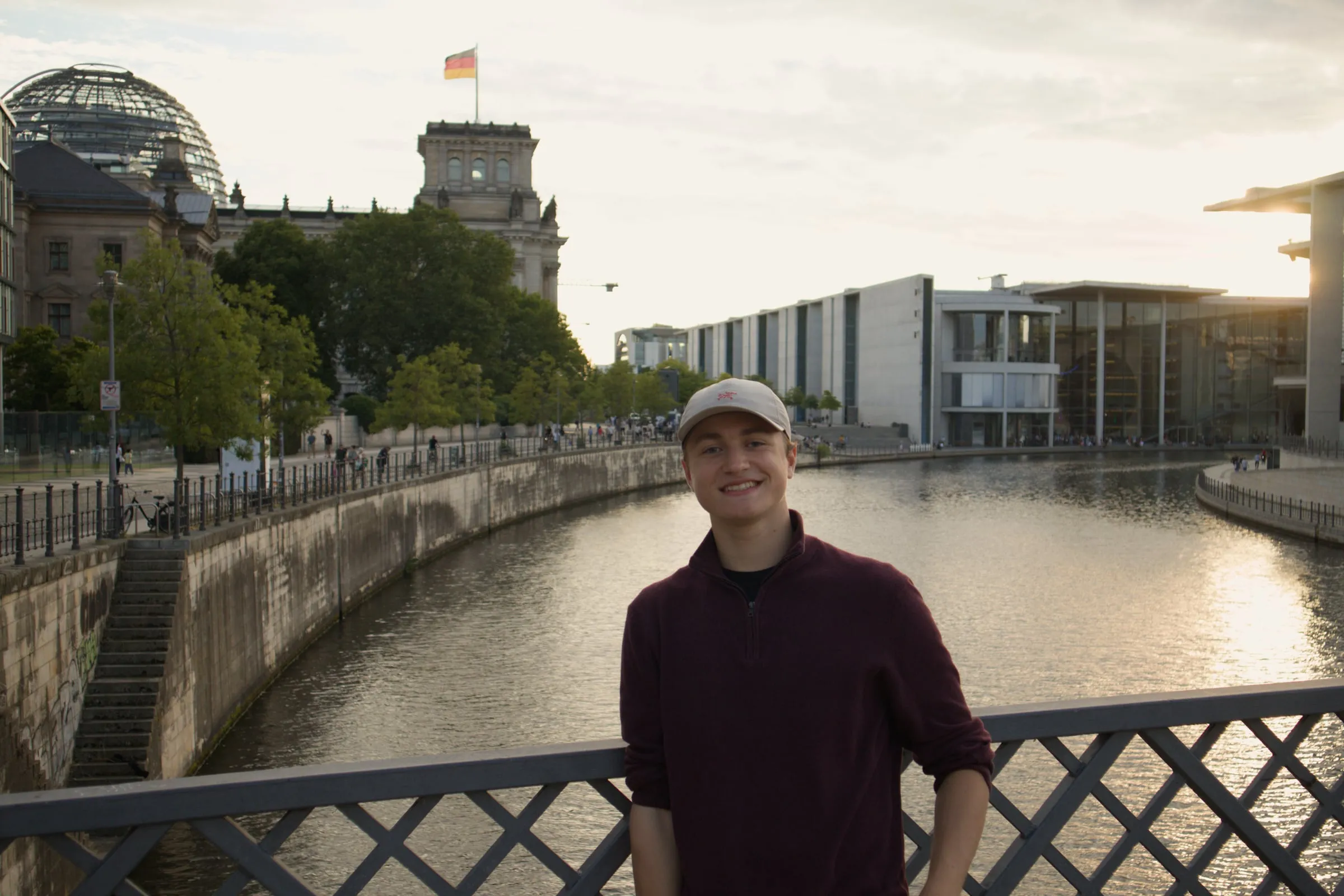 James smiling on a bridge over the River Spree with parliament in the background